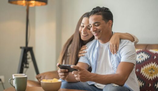 Happy young happy couple using smartphone social media apps at home, smiling husband and wife
