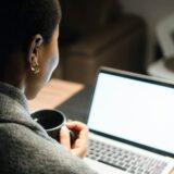Young black woman, holding cup of coffee, looking at computer screen