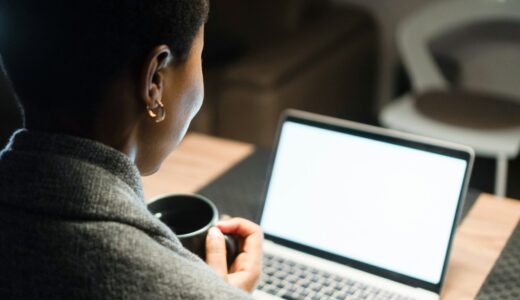 Young black woman, holding cup of coffee, looking at computer screen
